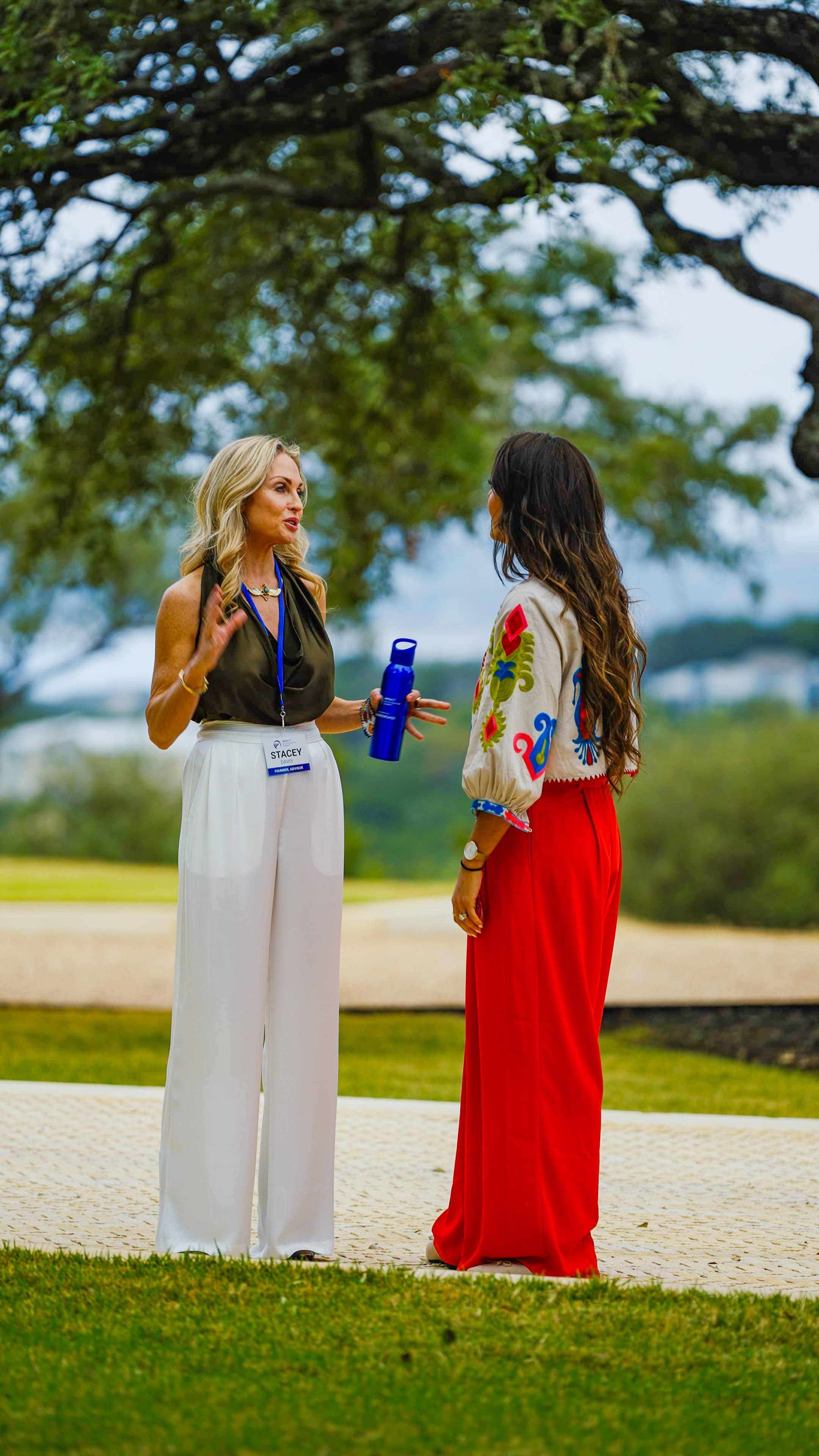 Two female participants in conversation on pathway under large tree