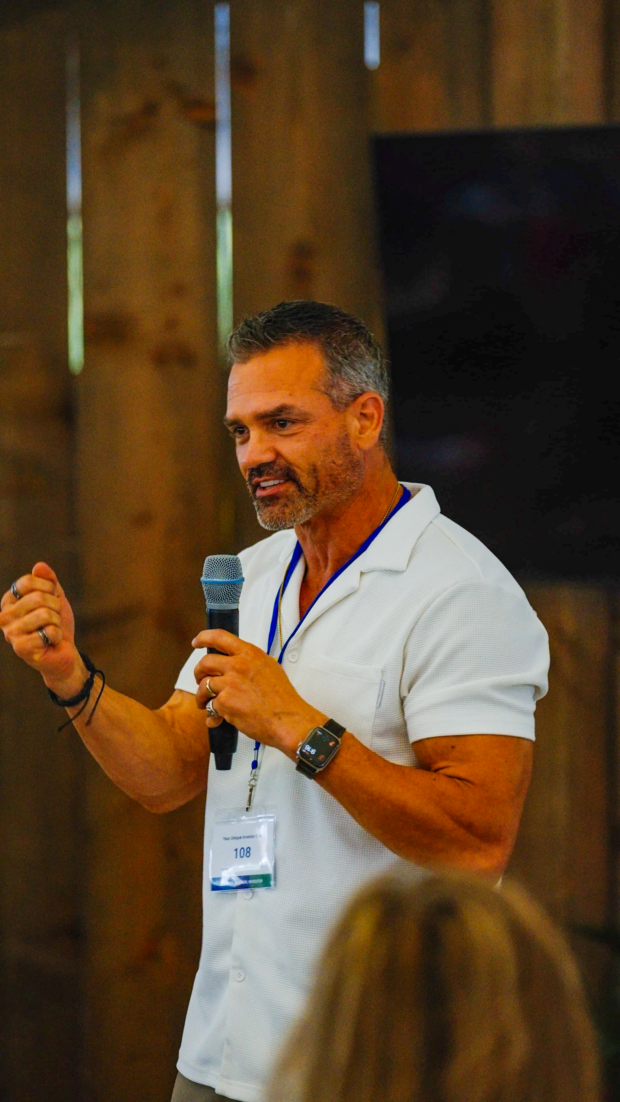 Male participant speaking with microphone indoors, gesturing with hand